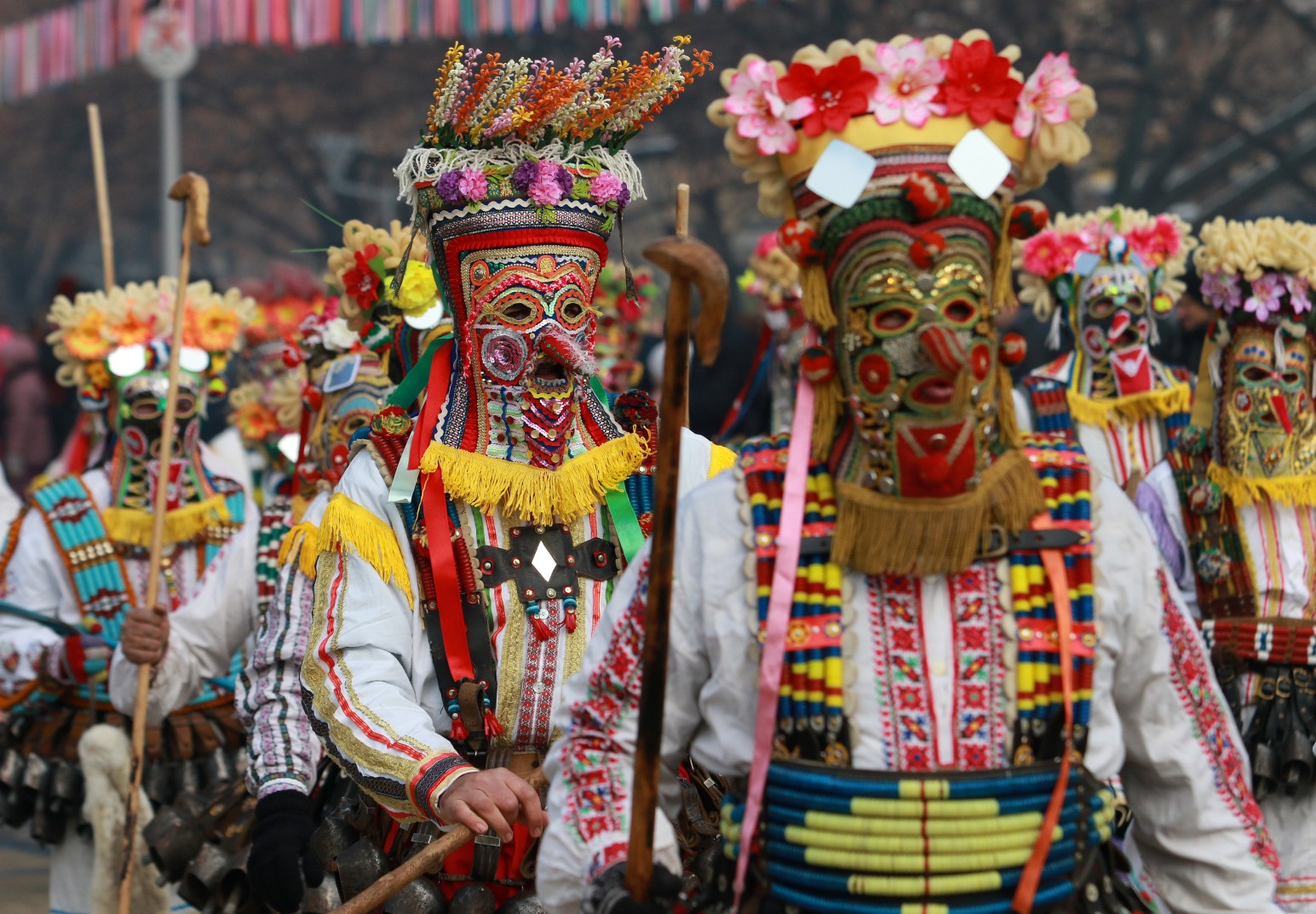 Kukeri performers in elaborate flower-covered masks and bell-adorned costumes at a traditional Bulgarian festival