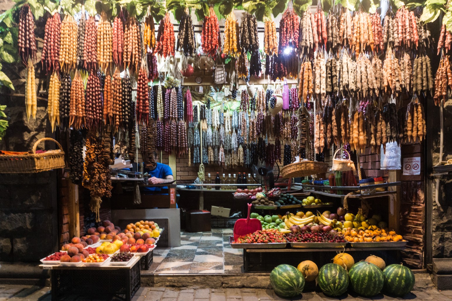 Market stall hung with rows of colourful churchkhela alongside baskets of fresh fruit and watermelons