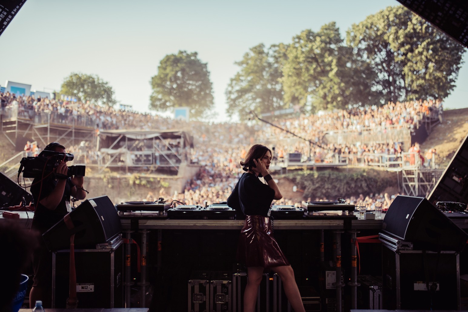 A DJ performing on stage at EXIT Festival in the Petrovaradin Fortress moat in Novi Sad, with a large crowd filling the amphitheatre