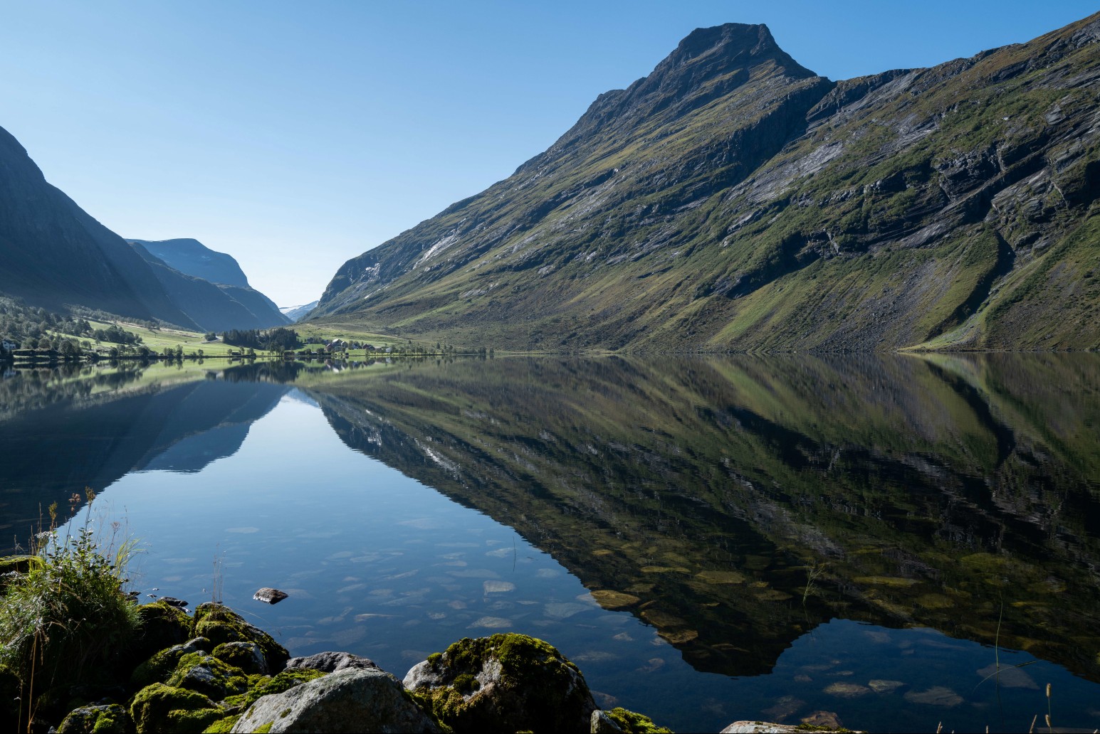 A still mountain lake reflecting steep green and rocky peaks in Norway