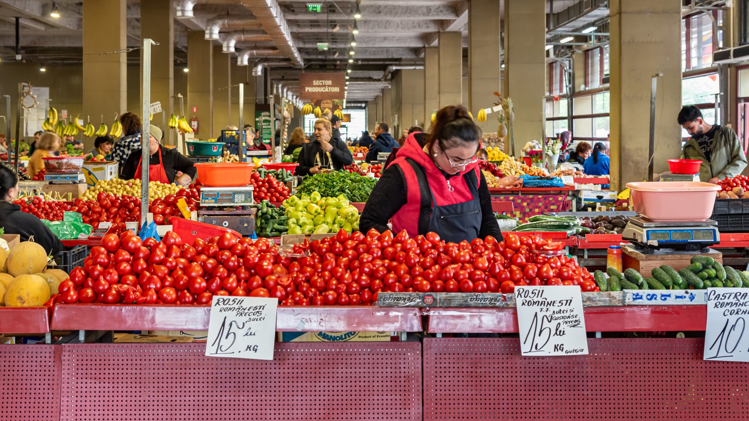 A vendor arranging piles of fresh tomatoes and vegetables at a stall in Bucharest’s Obor Market