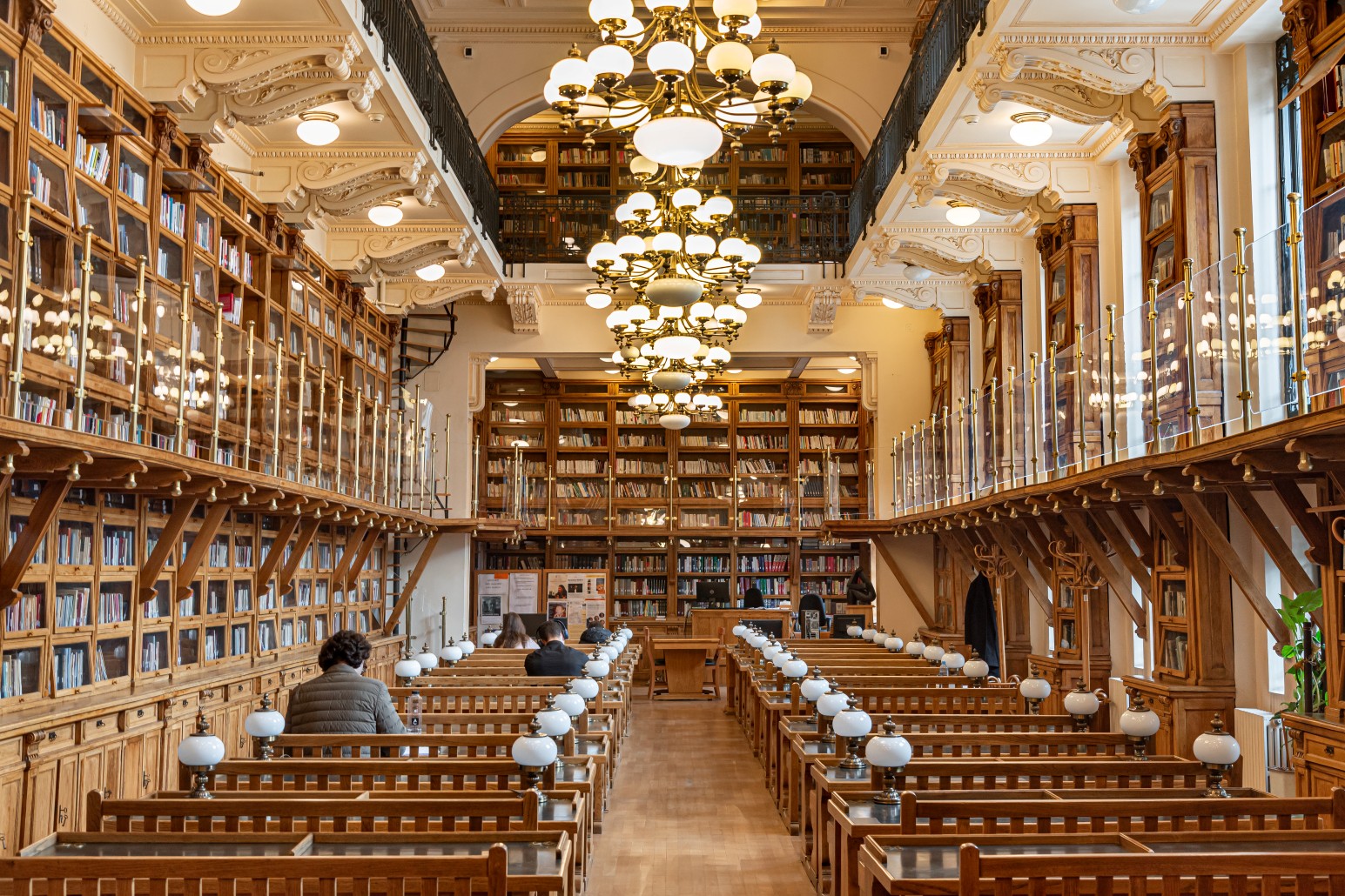 The ornate reading room of the University of Bucharest’s Faculty of Letters library, with wooden bookshelves, brass chandeliers, and students studying at long desks
