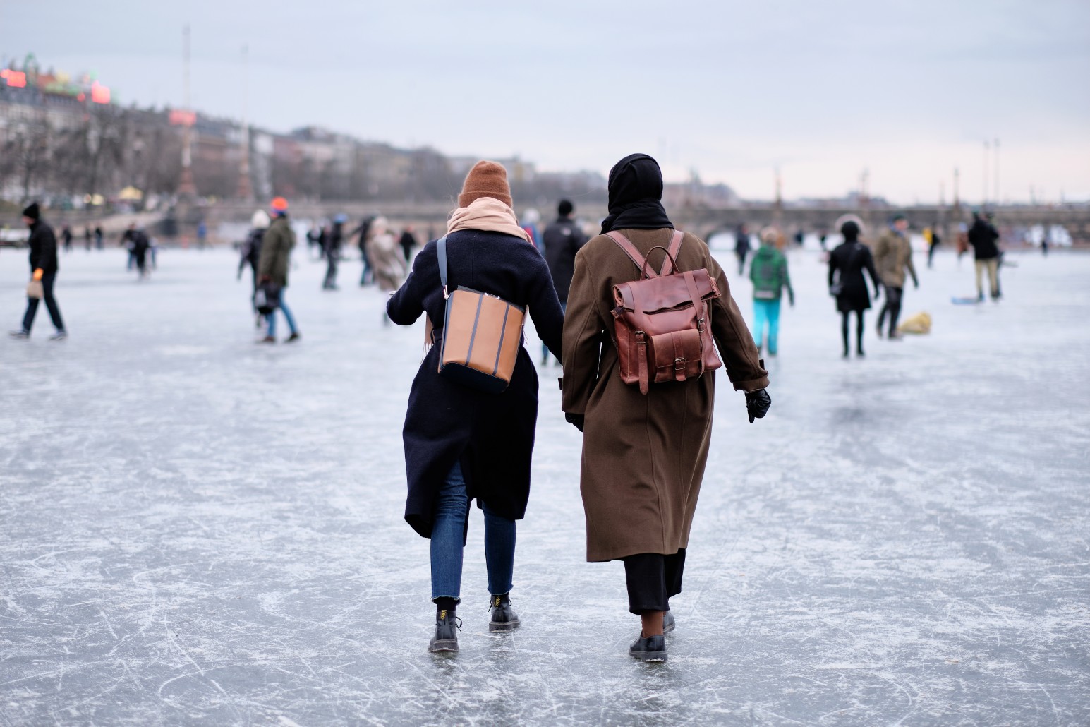 People walking and skating across a frozen lake in Copenhagen, Denmark, with the city skyline in the background