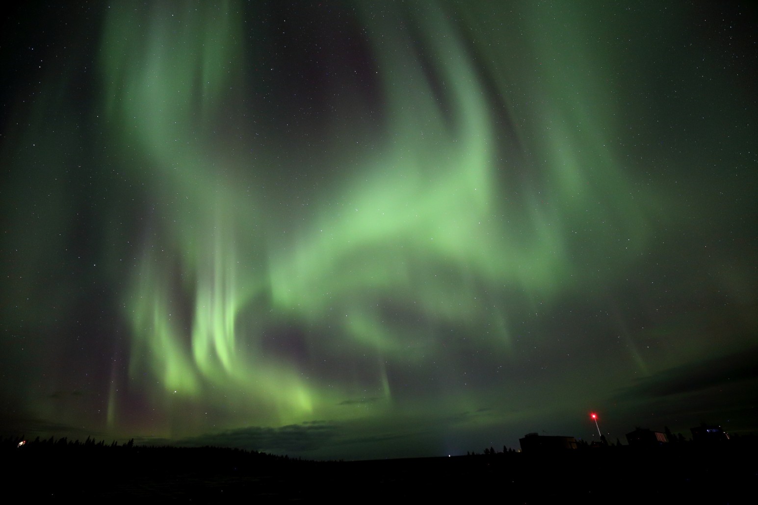 The northern lights glowing green over the dark skyline of Kiruna, Sweden