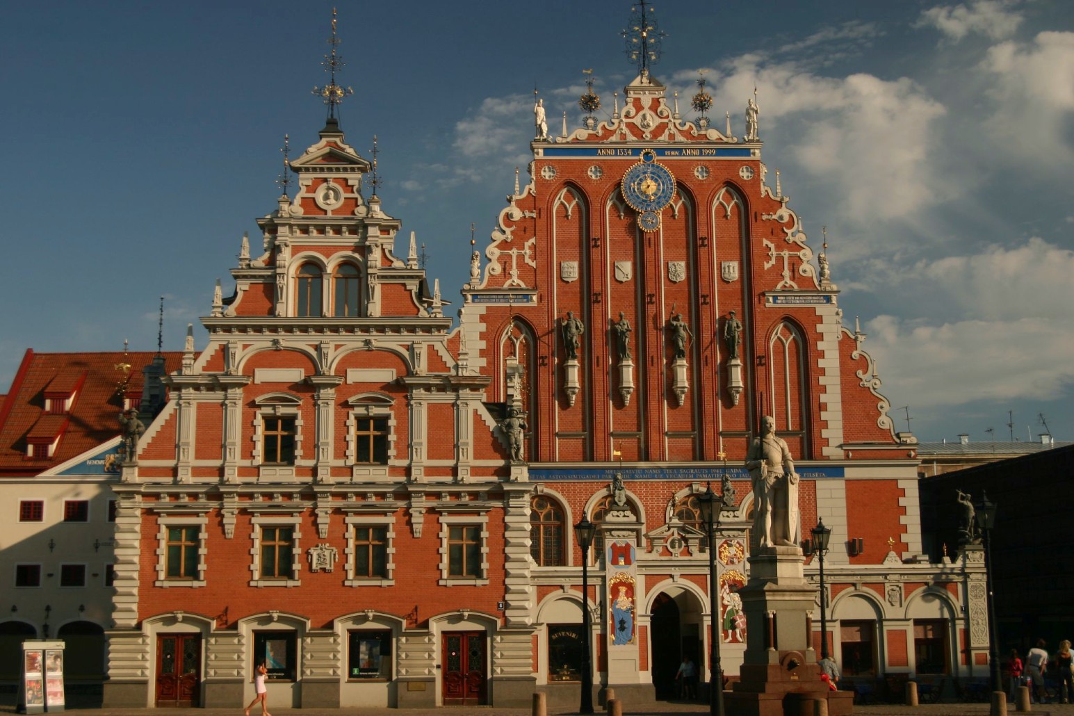 The ornate red-brick Gothic facade of the House of the Blackheads in Riga's Town Hall Square, with an astronomical clock and rooftop statues against a blue sky.