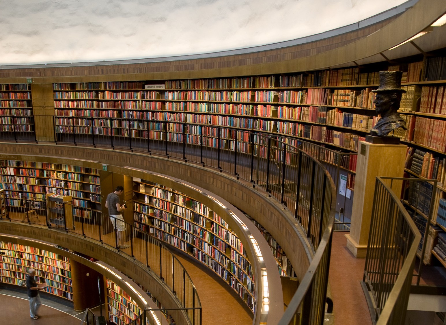 The curved, multi-level bookshelves of Stockholm City Library, with a bronze bust on display