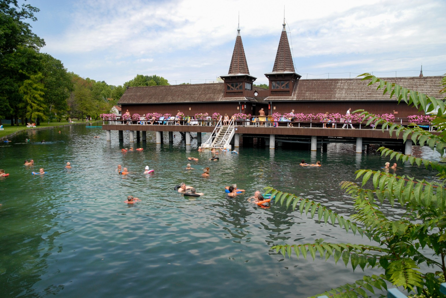 Lake Hévíz thermal spa, with a wooden bath house featuring twin turrets on stilts over the water and people swimming and relaxing on floats