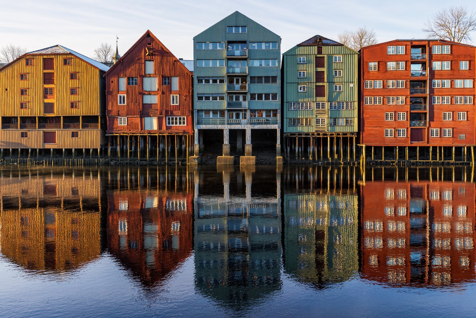 Colourful wooden warehouses on stilts reflected in the river in Trondheim, Norway