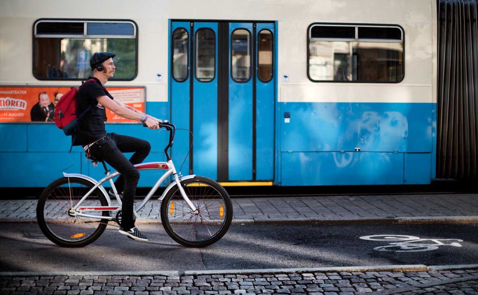 A cyclist riding past a blue and white tram on a cobbled street in Gothenburg, Sweden