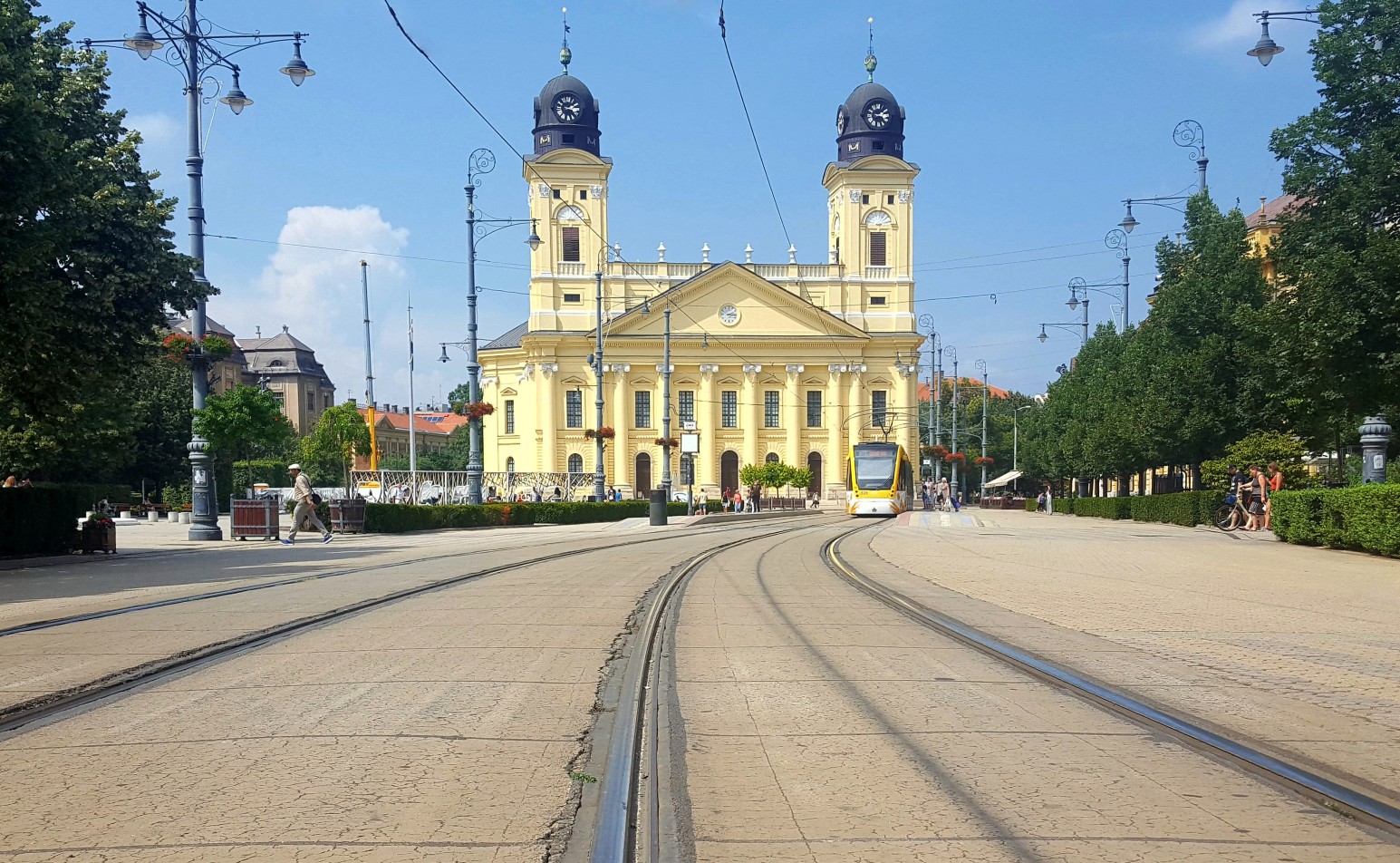 The Great Church in Debrecen’s main square, a yellow neoclassical building with twin clock towers, with a tram approaching along the tracks