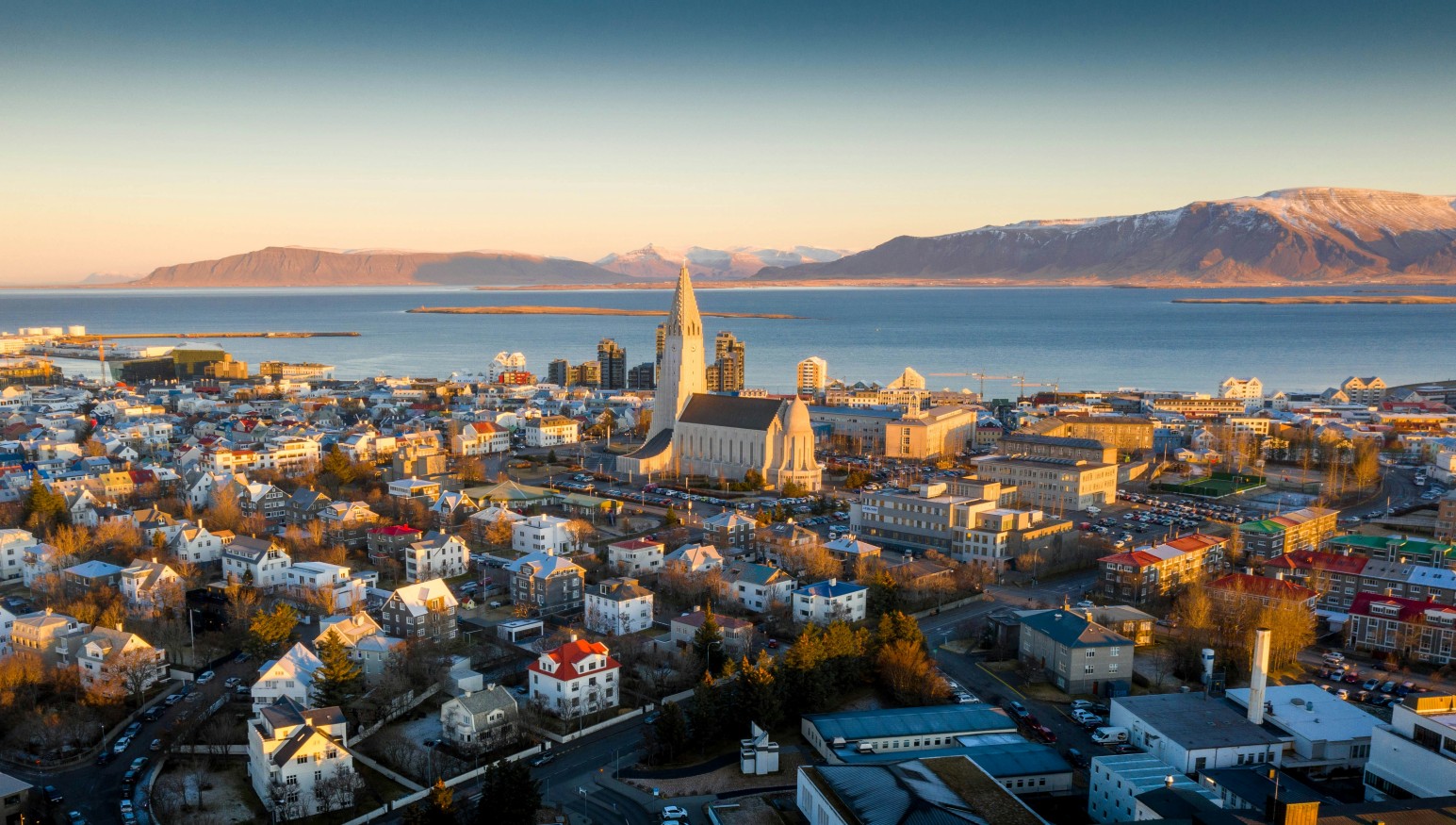 Aerial view of Reykjavík at sunset, with Hallgrímskirkja church tower rising above the colourful rooftops and mountains beyond