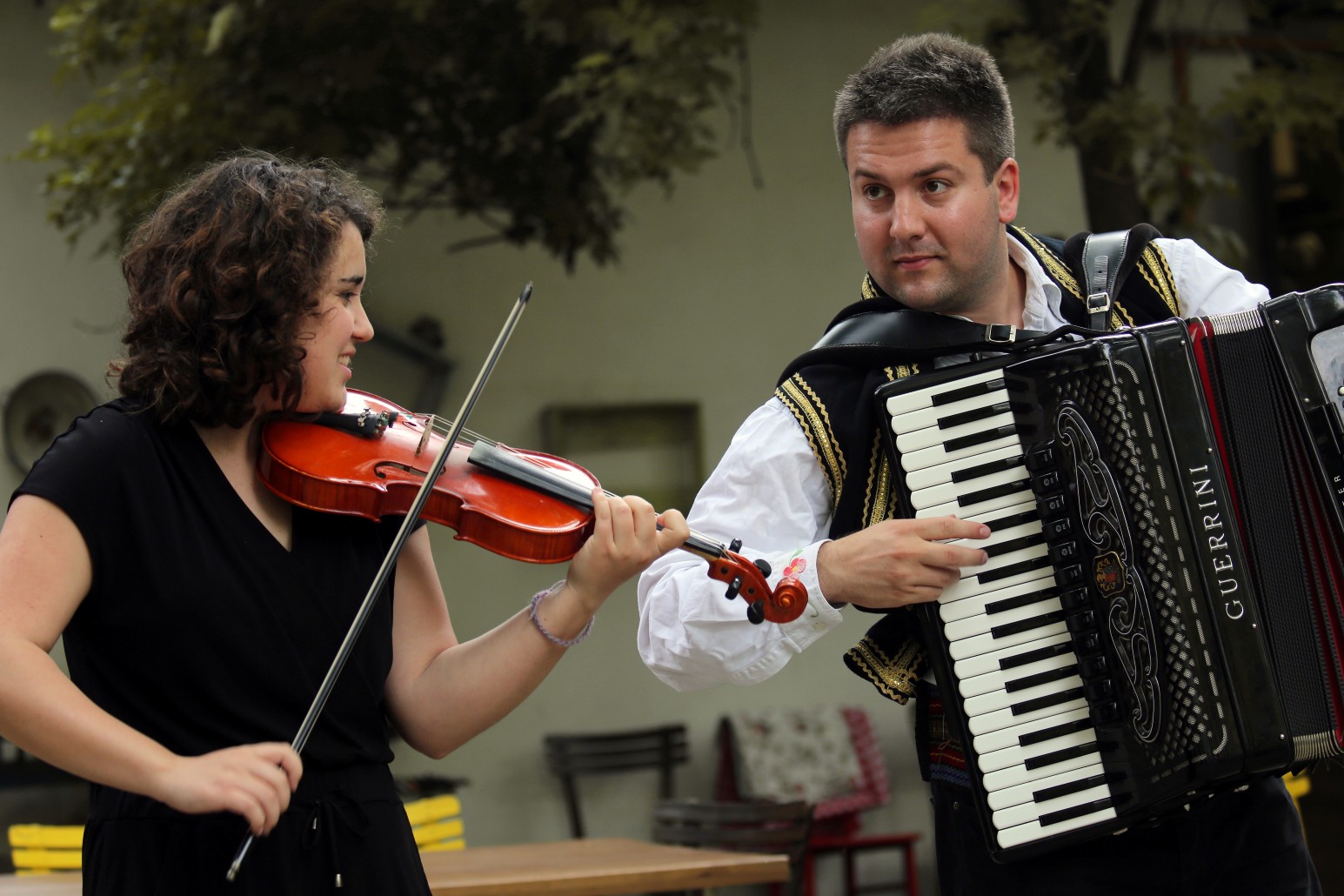 A violinist and an accordion player in traditional Serbian folk costume performing together outdoors
