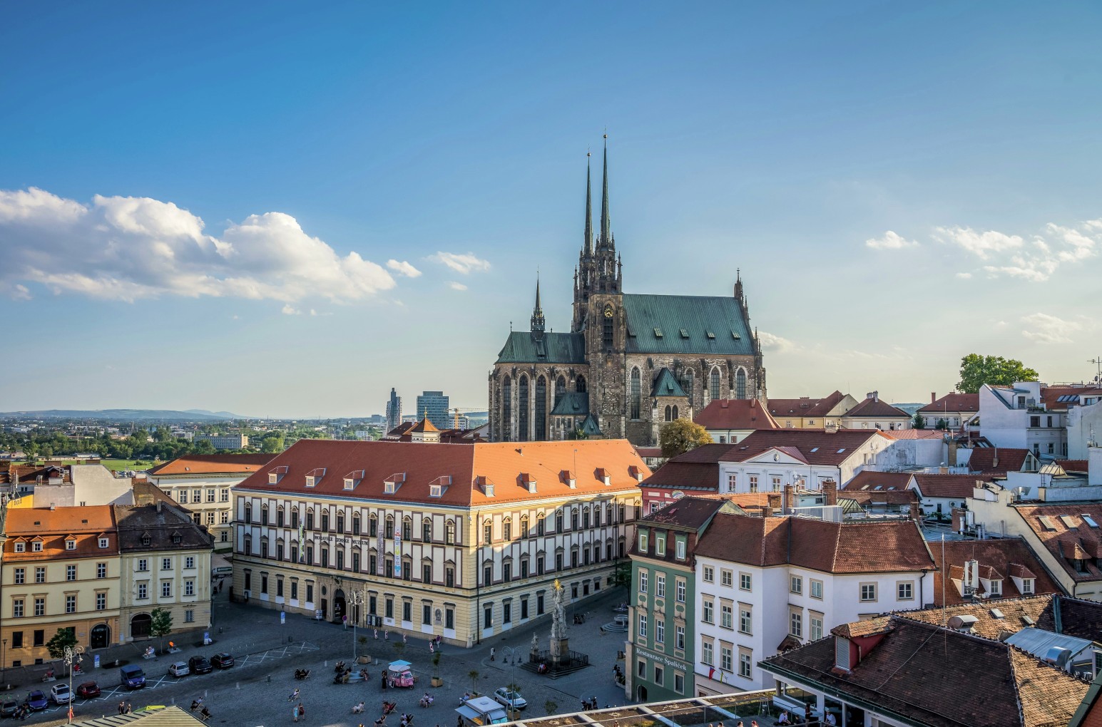 An elevated view of Brno's old town, with the twin Gothic spires of St. Peter and Paul Cathedral rising above red-tiled rooftops.