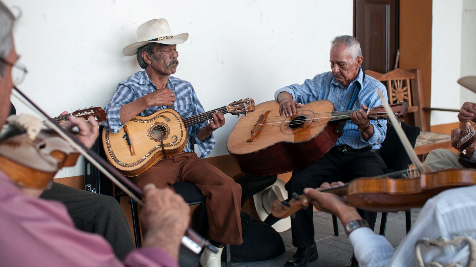 A group of older musicians playing guitars, a violin and a guitarrón together outdoors in Nayarit