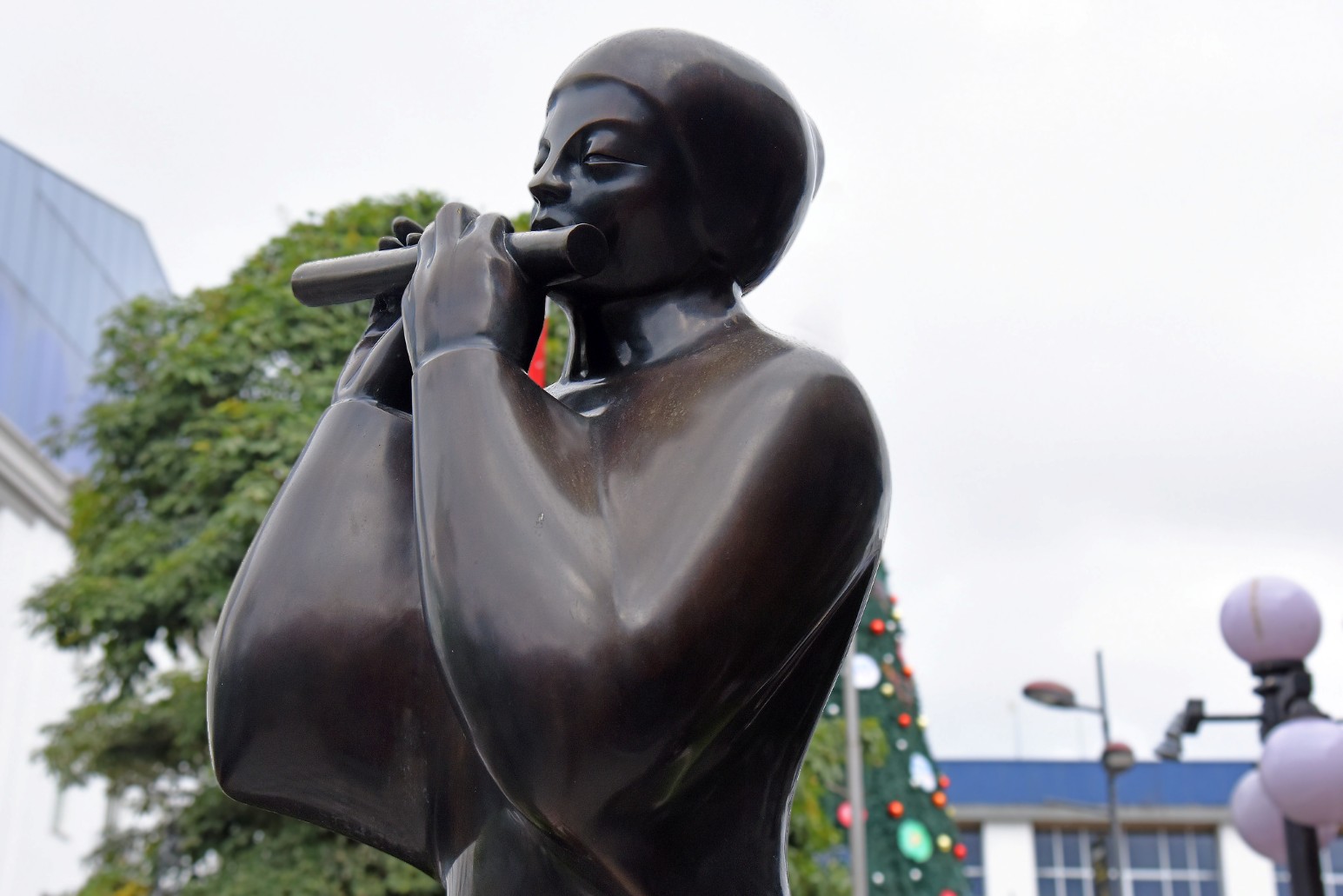 Bronze statue of a woman playing a flute in central San José, with a decorated Christmas tree in the background