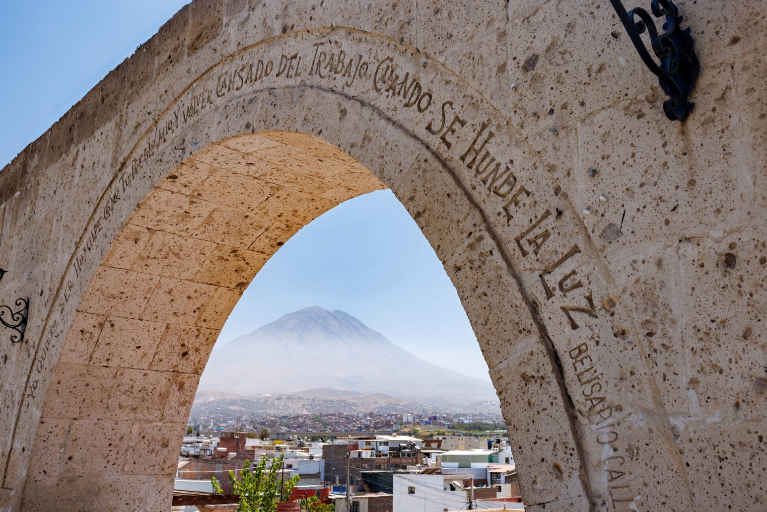 A stone archway framing a view of a volcano over the rooftops of Arequipa