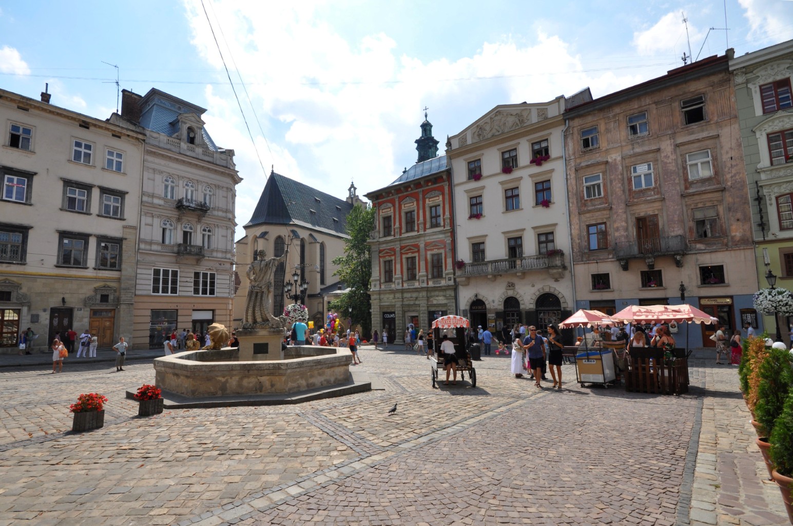 A historic square in Lviv's old town with a fountain, statue and surrounding period buildings