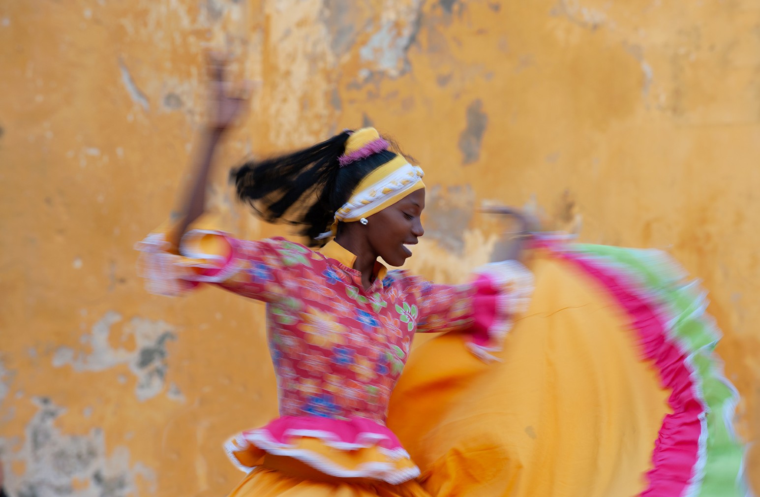 A dancer in a bright traditional dress twirling against a weathered orange wall in Cartagena