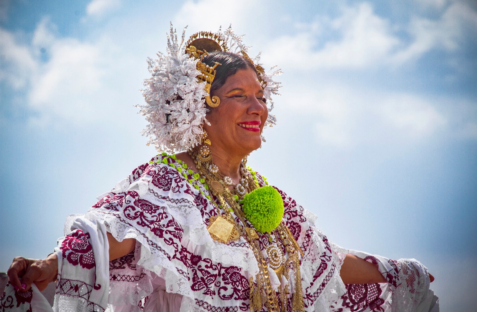 A woman in a traditional embroidered pollera dress and gold headpiece dancing against a bright blue sky