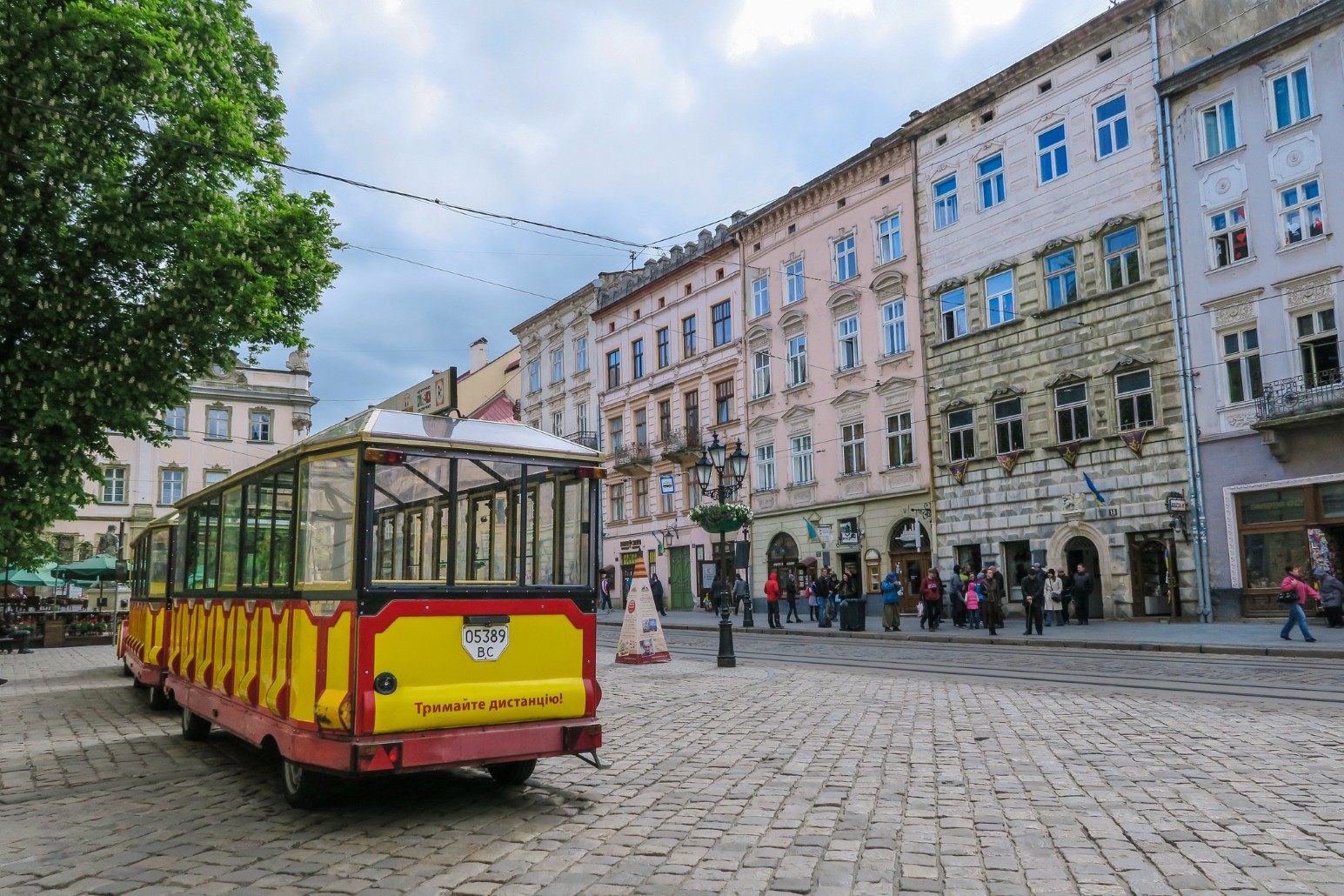 A yellow tourist tram travelling past pastel-coloured historic buildings in Lviv's old town
