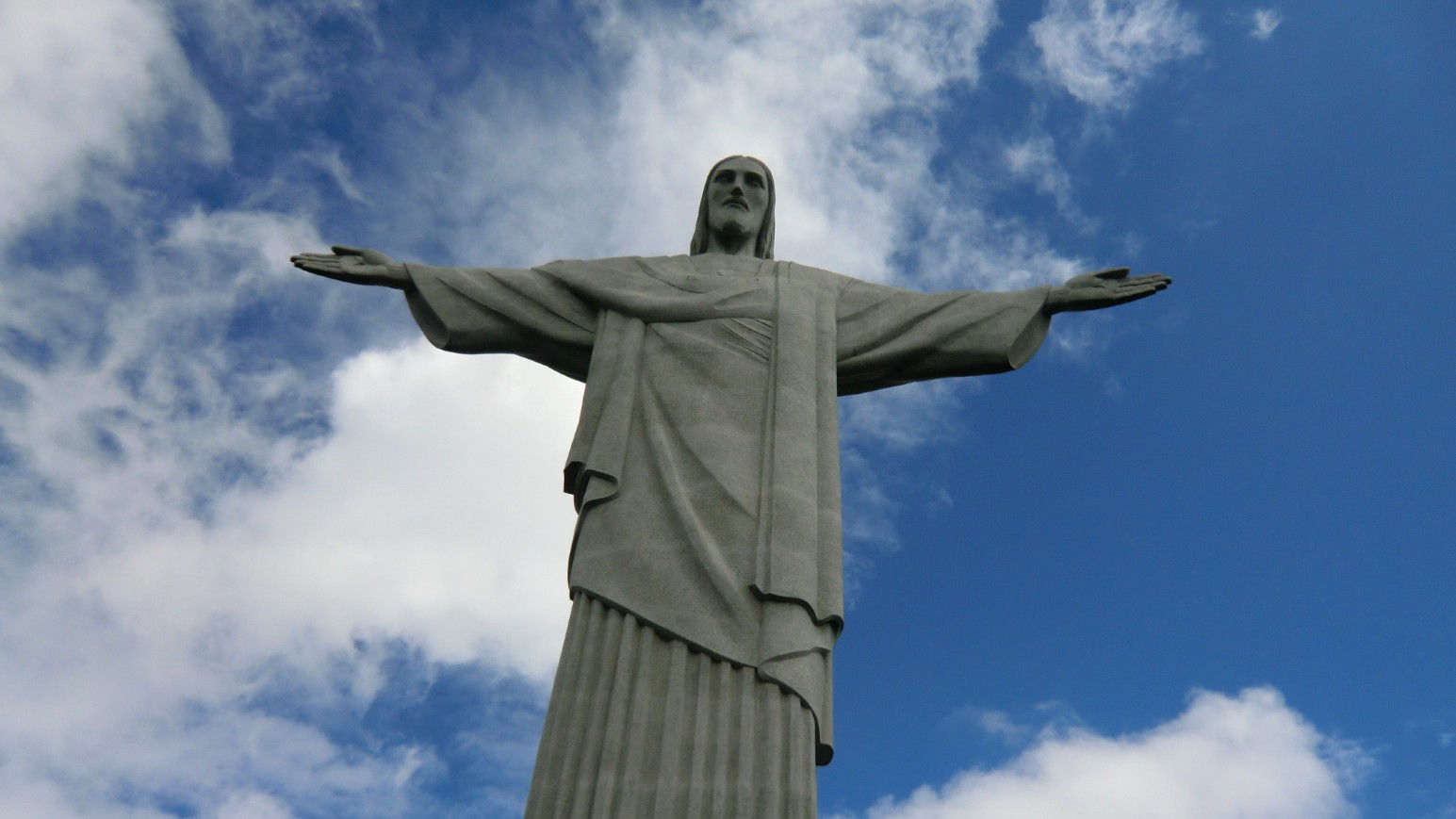 The Christ the Redeemer statue in Rio de Janeiro pictured from below against a blue sky with clouds