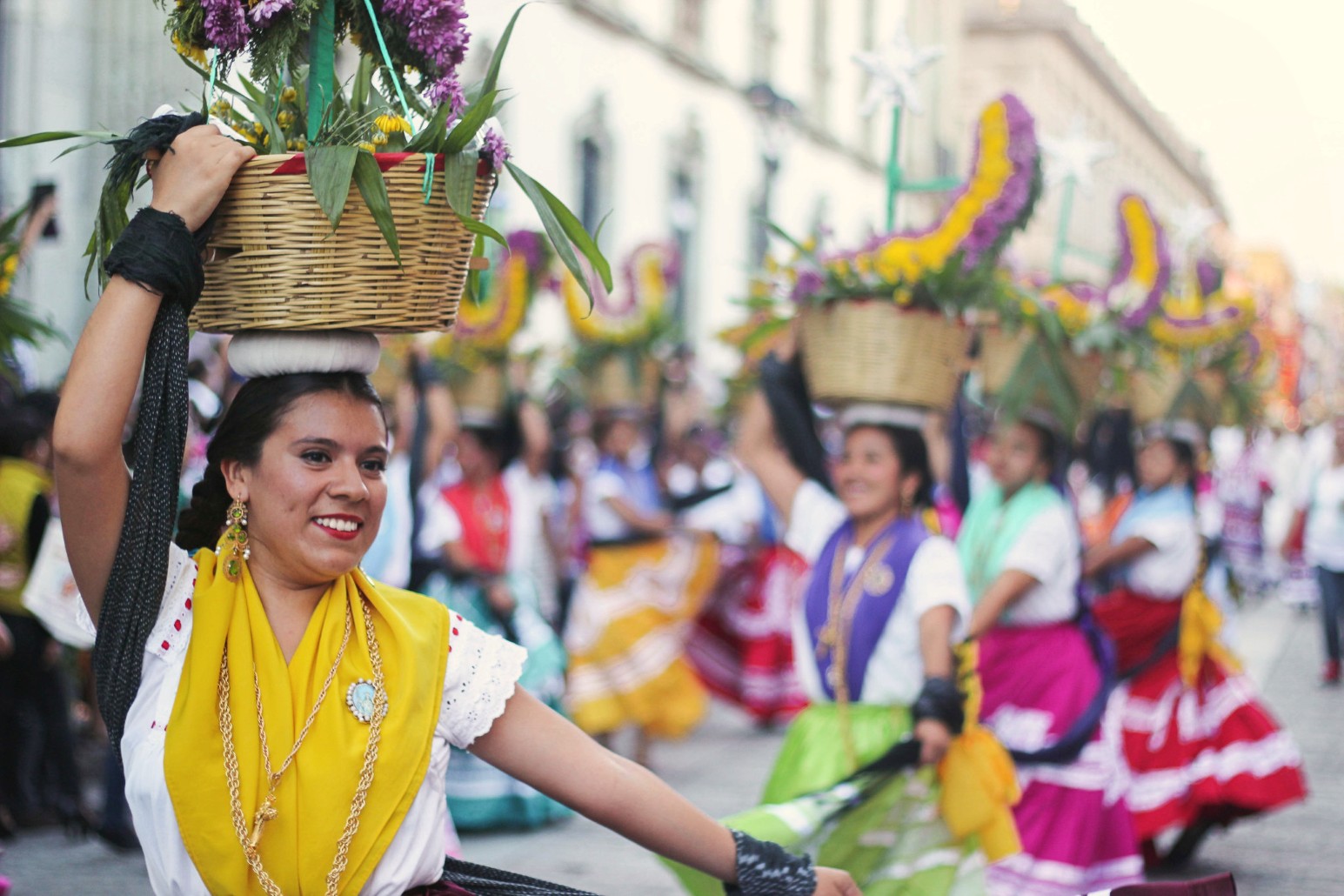 Dancers in traditional Oaxacan dress carrying flower-filled baskets on their heads during a street parade