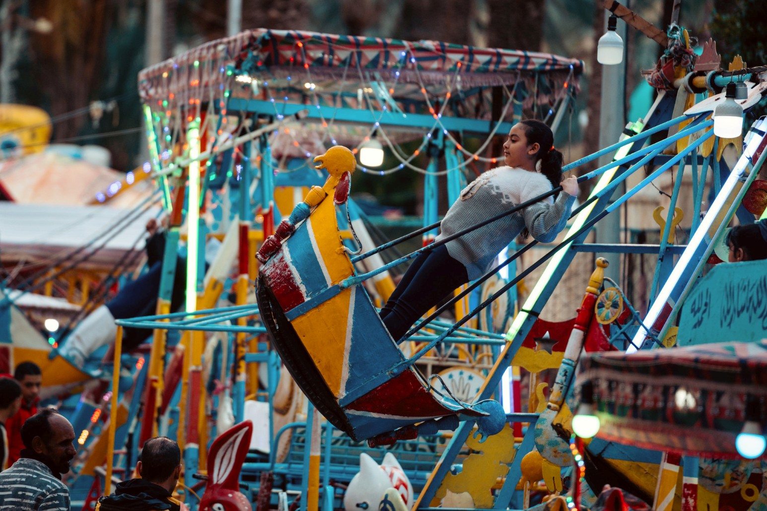 Girl riding a brightly painted swing boat ride strung with fairy lights at an amusement park in Alexandria, Egypt
