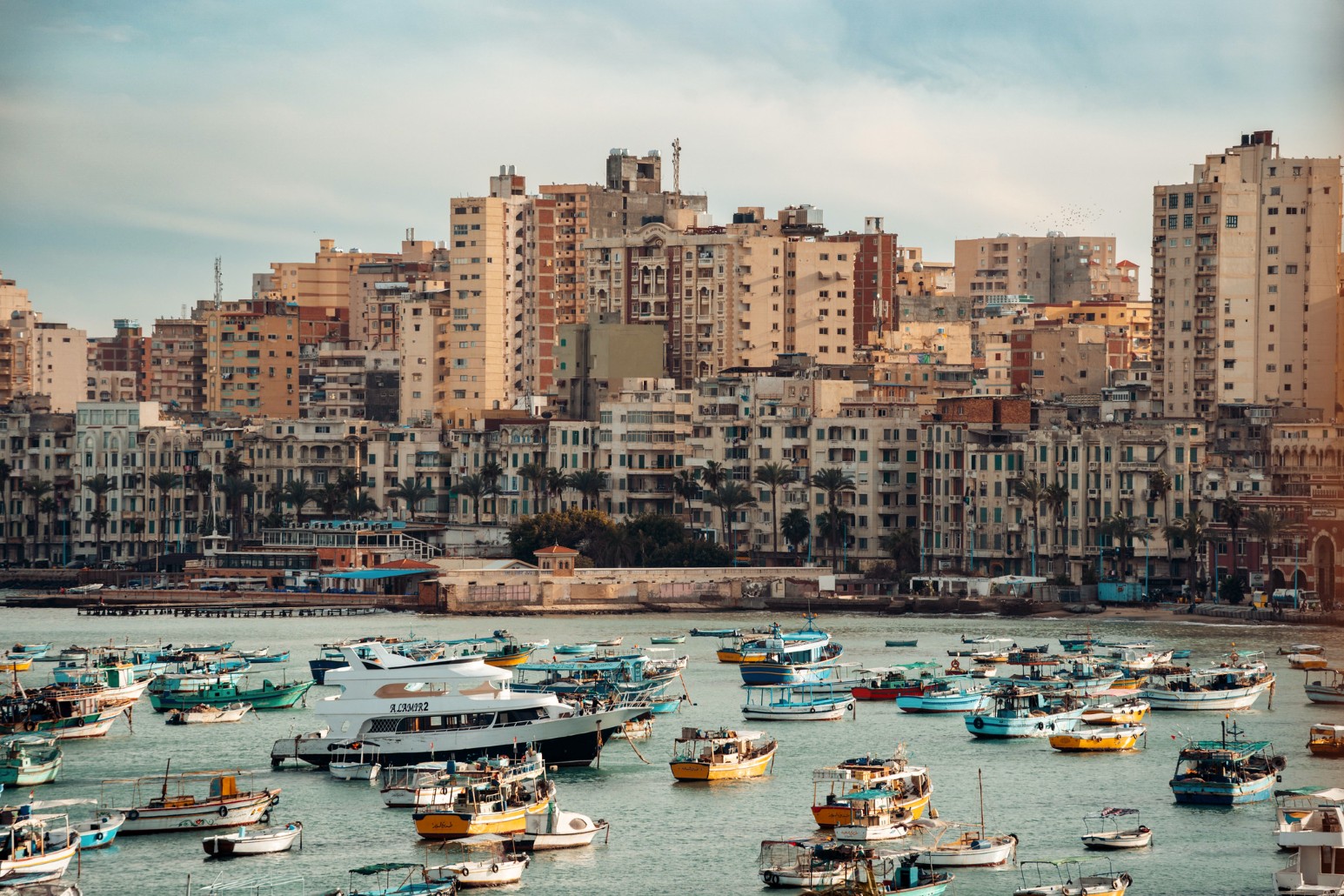 Colourful fishing boats moored in the harbour in front of seafront apartment blocks in Alexandria, Egypt