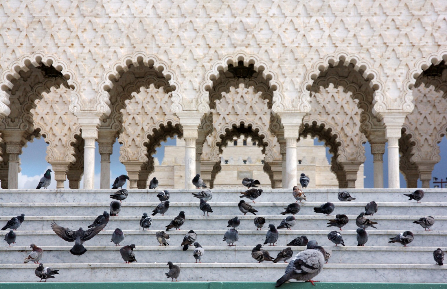 Pigeons gathered on white marble steps in front of ornately carved Moorish arches at the Mausoleum of Mohammed V in Rabat, Morocco