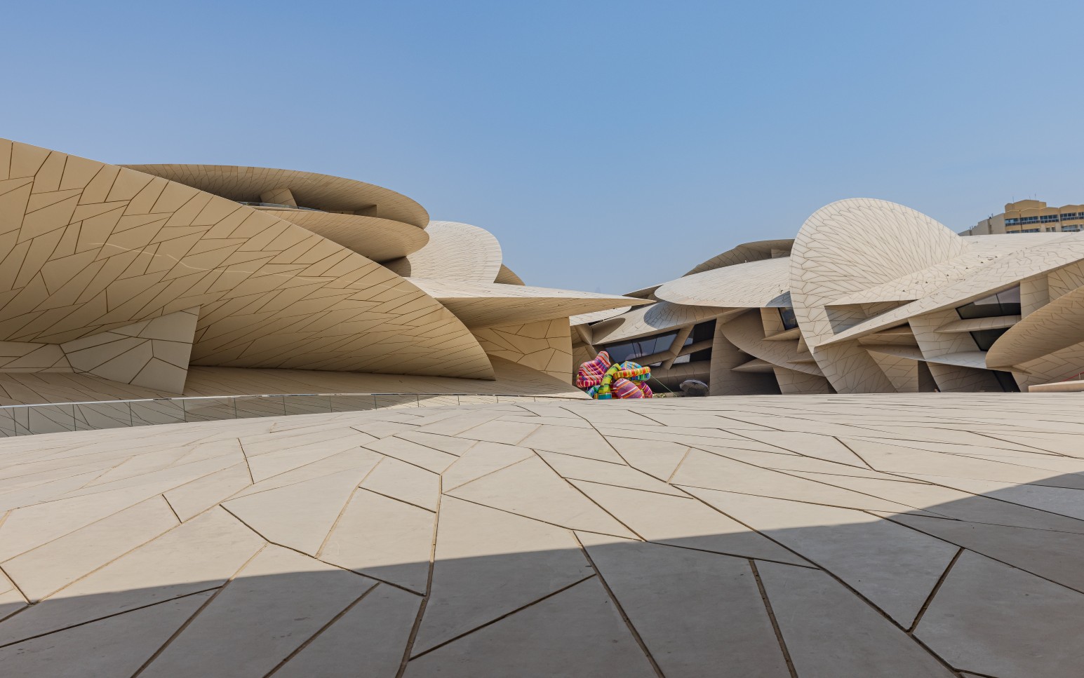 The interlocking disc-shaped walls of the National Museum of Qatar in Doha, designed to resemble a desert rose, with a colourful sculpture visible between the curved structures