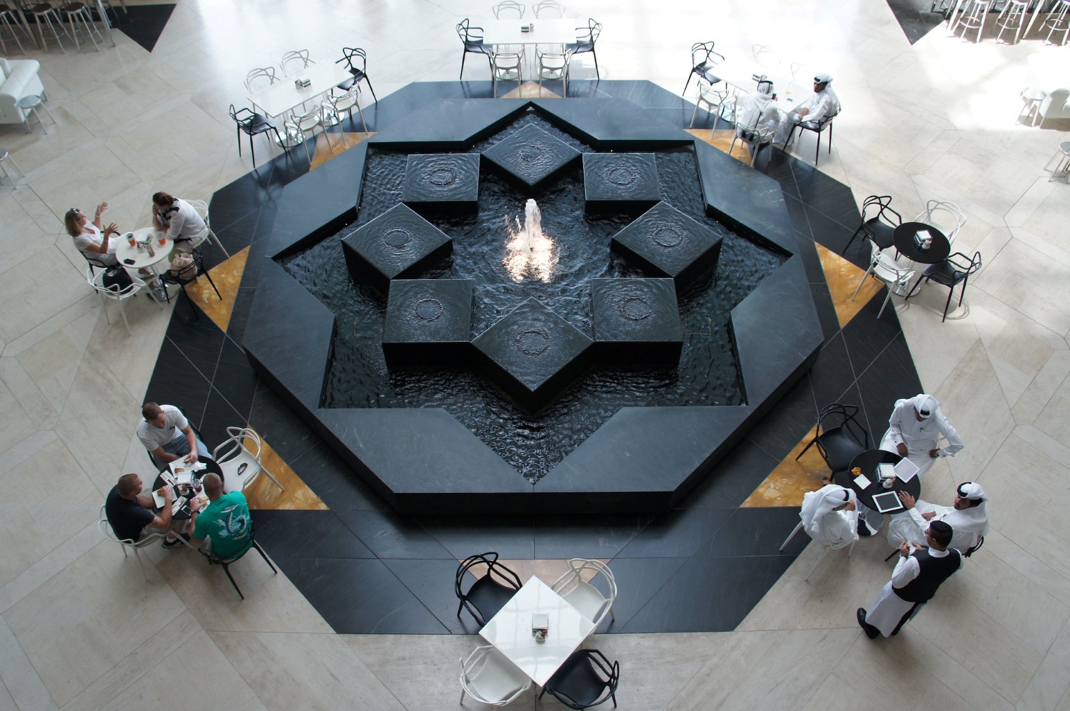 An overhead view of an indoor café in Doha, Qatar, with people seated at tables around a black marble fountain shaped like an eight-pointed star